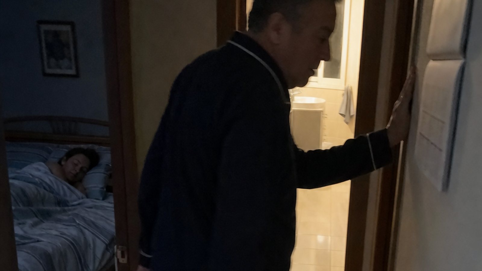Uomo maturo sveglio di notte davanti alla porta del bagno illuminata