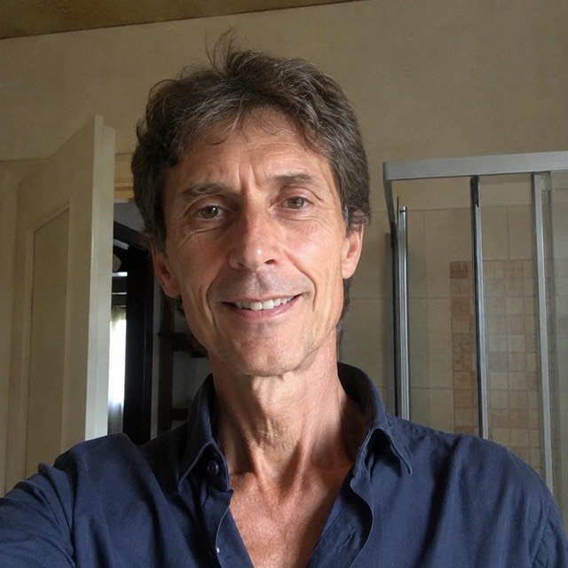 Ritratto di un uomo italiano asciutto sulla cinquantina, capelli sale e pepe, viso abbronzato, camicia blu navy